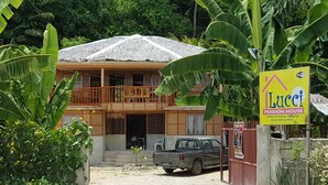 A two-story house with a thatched roof, a balcony, and a sign advertising a pension house. - Lucci Pension House (Alegria)