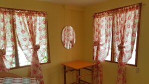 A room with two windows, a wooden chair, a mirror, and a bed with a patterned bedspread. - Lucci Pension House (Alegria)
