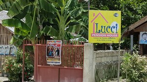 A gated entrance with a sign for a pension house, surrounded by lush greenery and a large banana tree. - Lucci Pension House (Alegria)