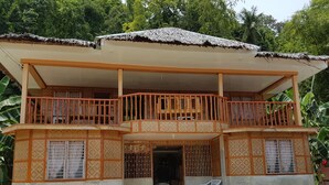 A two-story house with a balcony, a thatched roof, and a small porch area. - Lucci Pension House (Alegria)