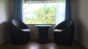 Um quarto com janela, duas cadeiras de vime e uma pequena mesa.