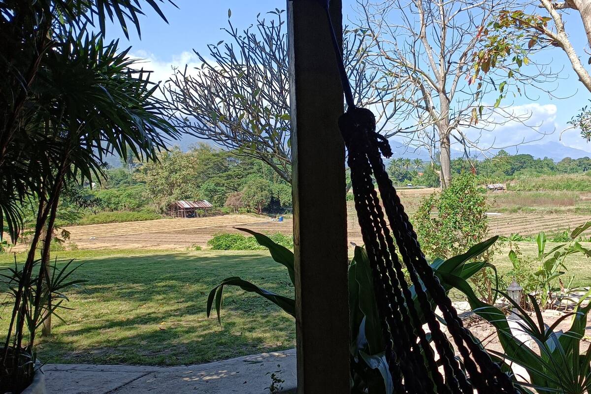A view from a covered area with a metal railing, overlooking a rural landscape with fields, trees, and a distant mountain.