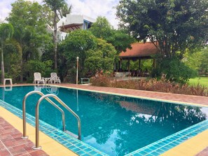 A swimming pool with clear blue water, surrounded by greenery and a gazebo.