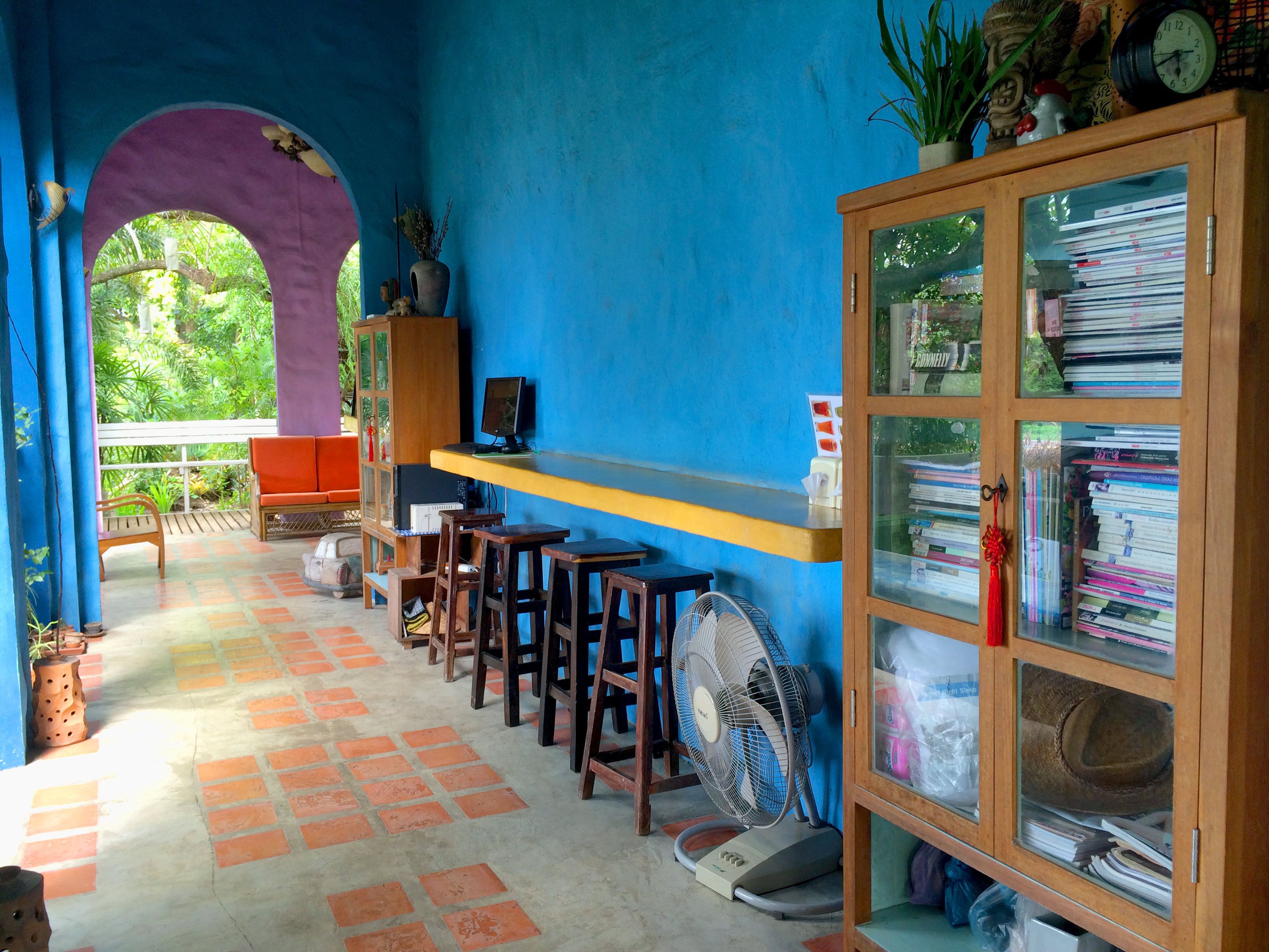 A room with a blue wall, a wooden cabinet with glass doors, a small table with a computer, and several wooden stools.