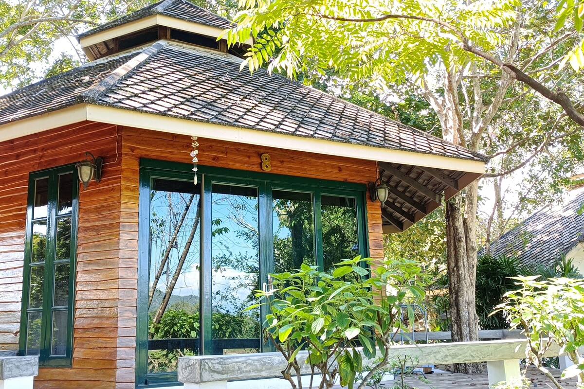 A wooden building with large windows and a tiled roof, surrounded by trees.