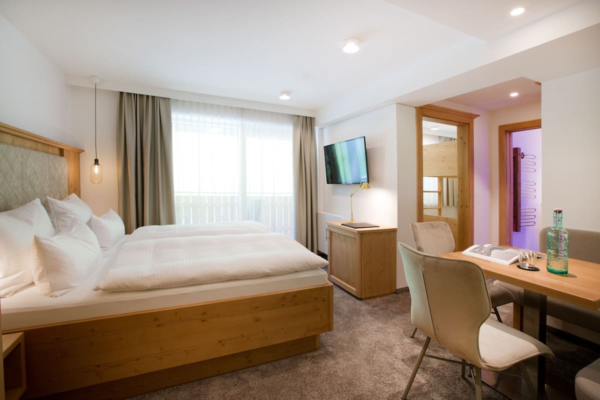 A hotel room with a double bed, a desk with a chair, a television, and a bottle on the table.
