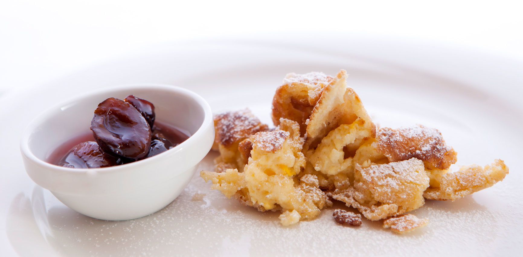 Un plato de postre con un bol de compota de fruta oscura y una pila de hojaldre desmenuzado espolvoreado con azúcar glas.