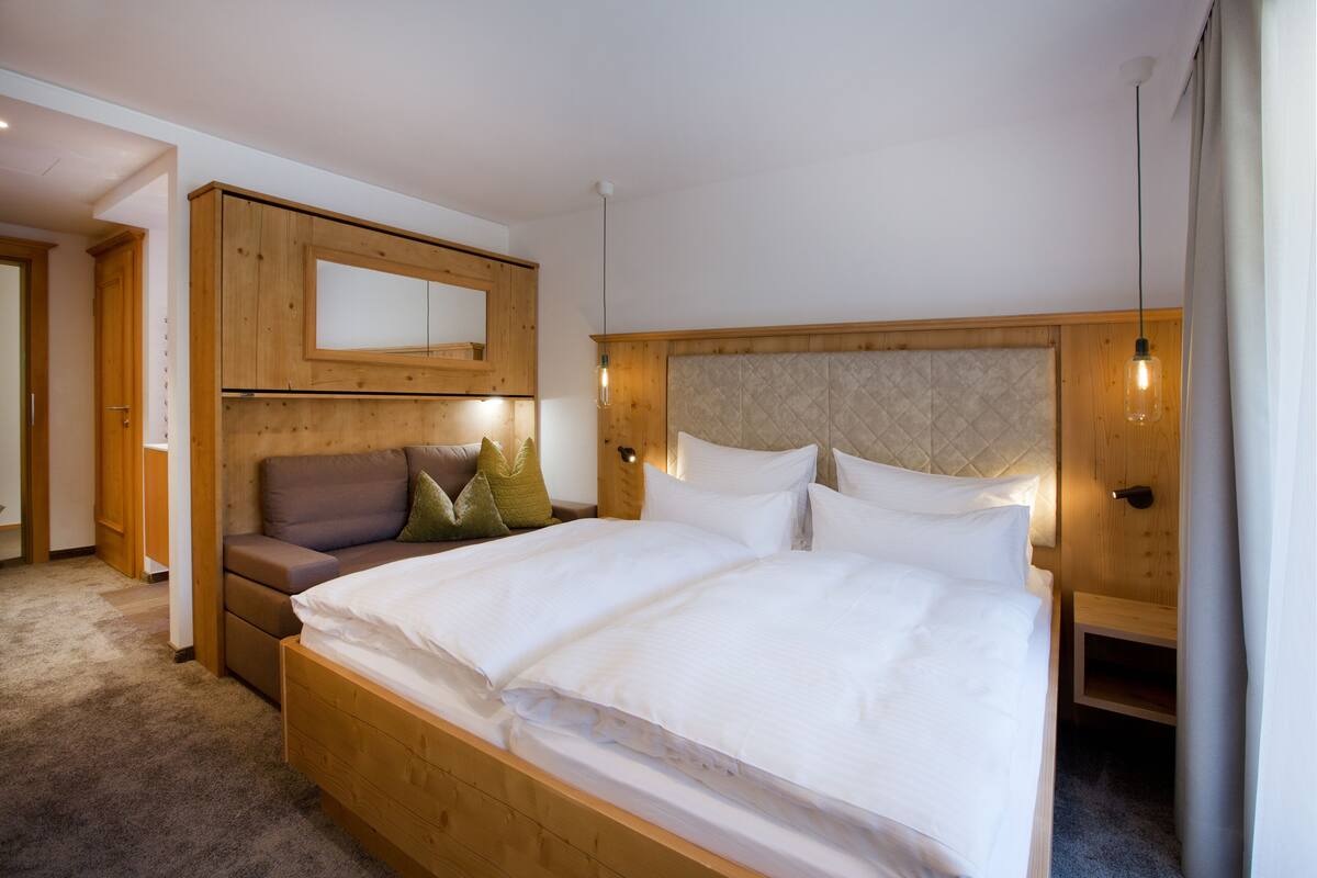 A bedroom with a wooden bed, a nightstand, a sofa, and a wall-mounted cabinet.