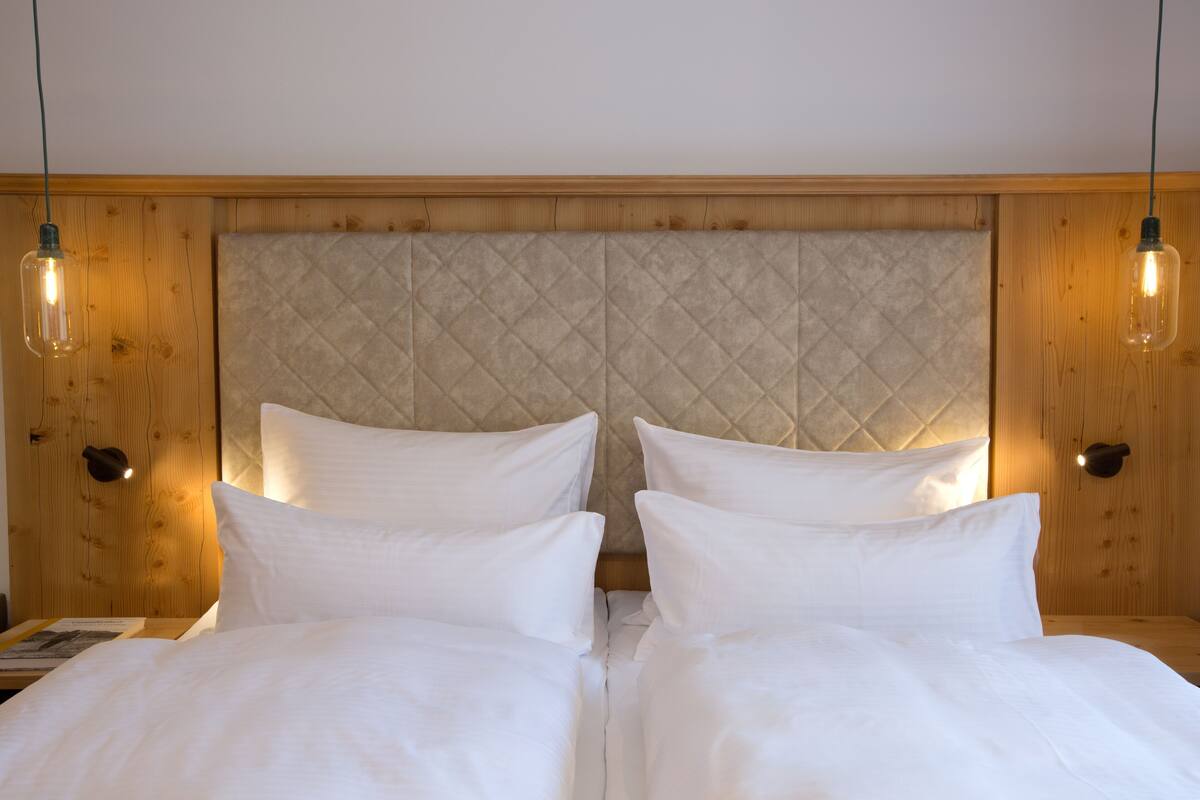 A double bed with a quilted headboard, two bedside lamps, and a wooden panel wall.