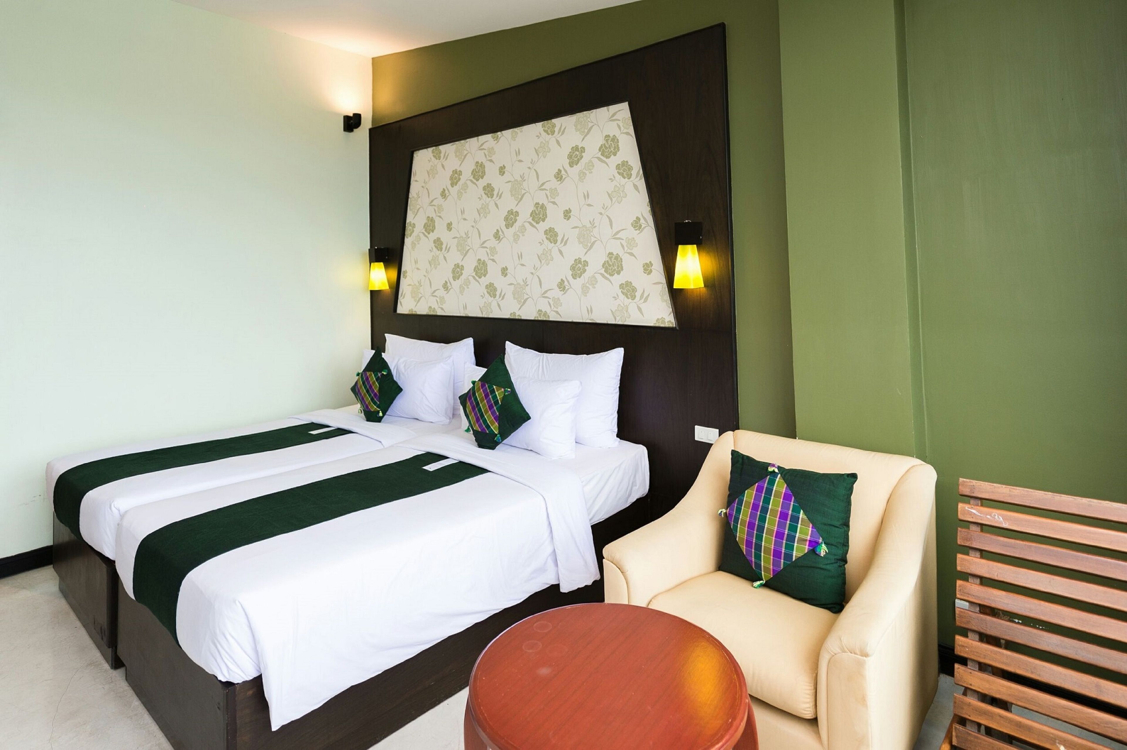 A hotel room with two beds, a sofa, a round table, and a decorative headboard.