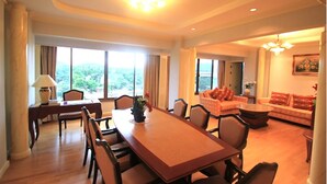A spacious hotel room with a large dining table, comfortable seating, a sofa, and a view of the outdoors. - River Kwai Hotel (Kanchanaburi)