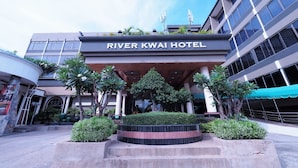 The River Kwai Hotel entrance with a covered walkway, palm trees, and a landscaped area. - River Kwai Hotel (Kanchanaburi)