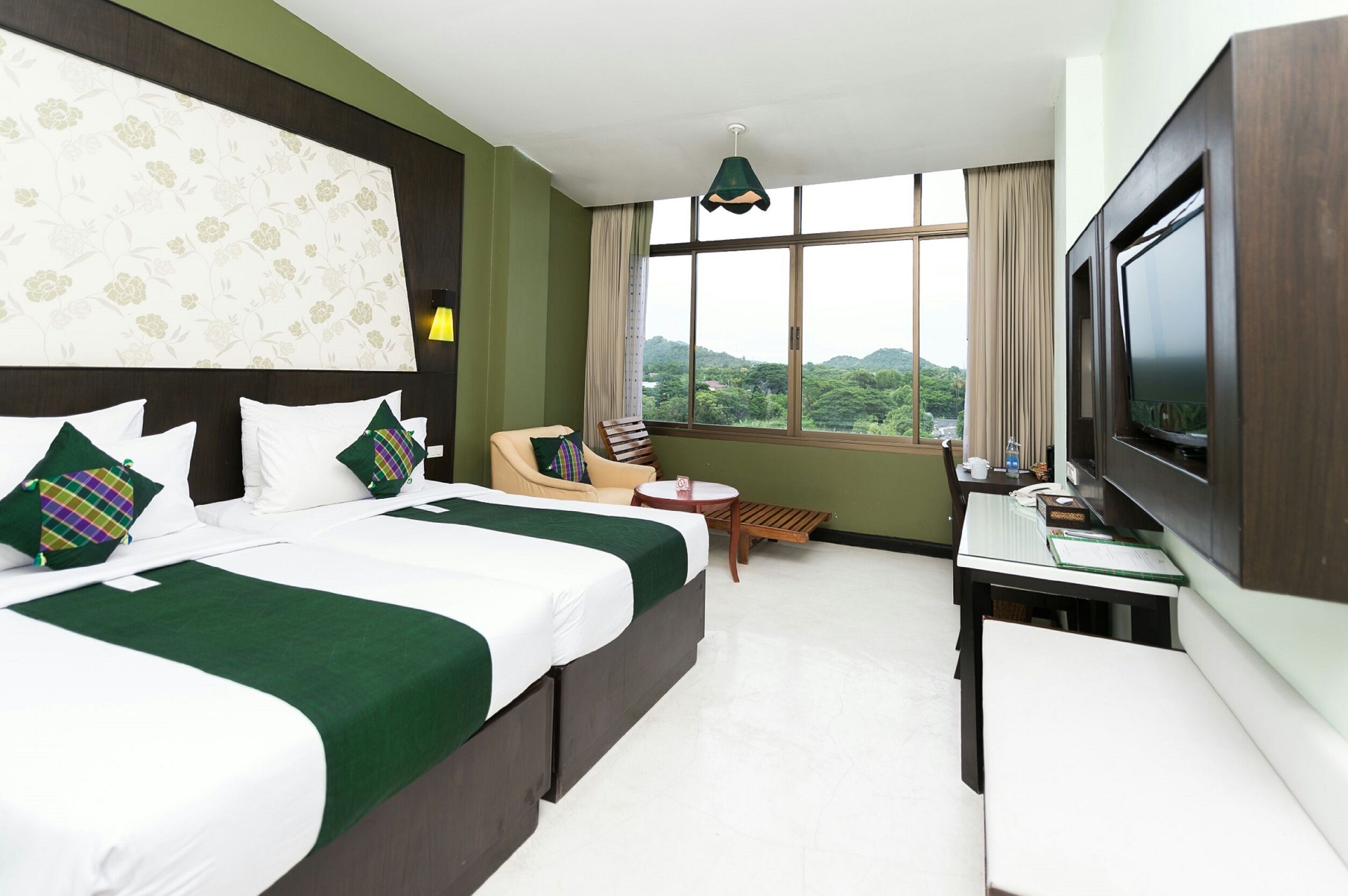 A hotel room with two beds, a TV, a desk, a chair, and a view of the outdoors.