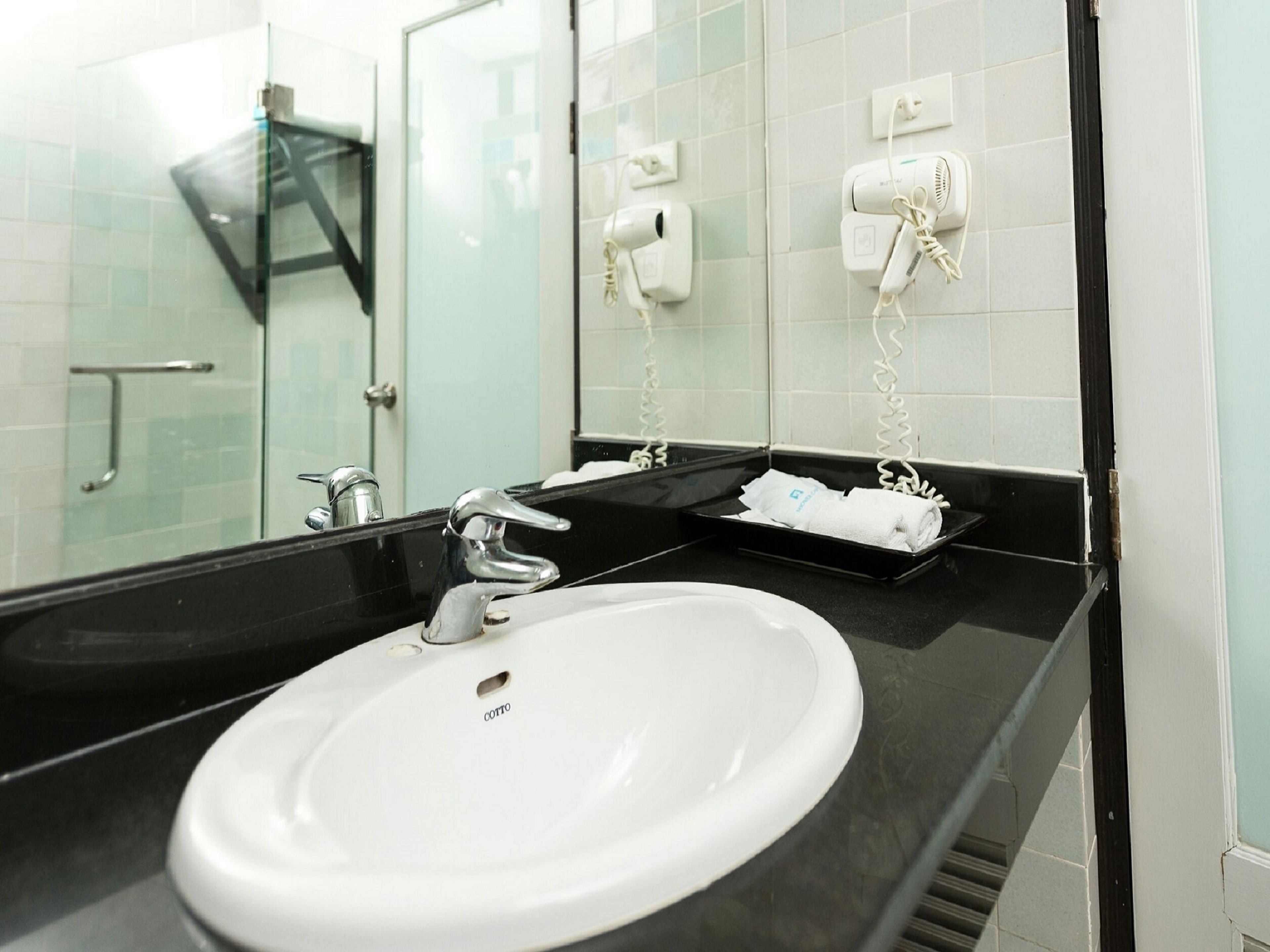 A hotel bathroom with a white sink, black countertop, and a glass shower enclosure.