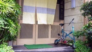 Un portón japonés tradicional con puertas correderas, una bicicleta y abundante follaje.