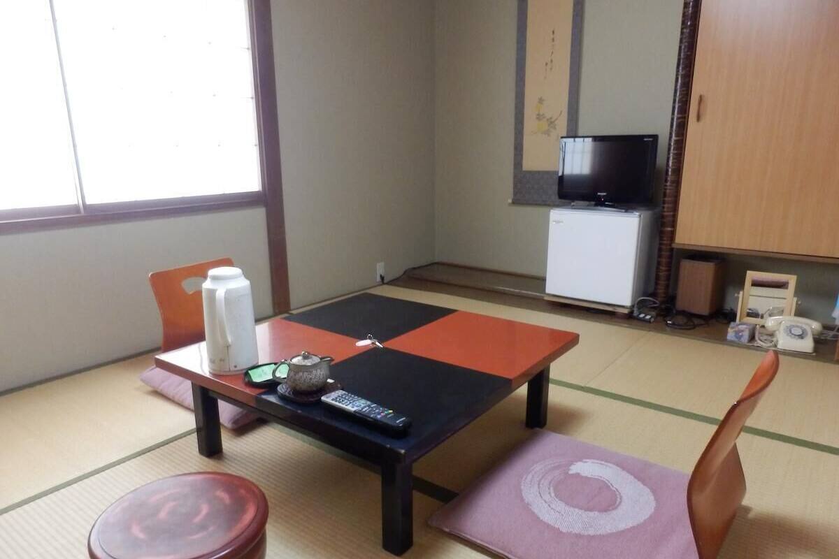 Quarto japonês tradicional com tatames, uma mesa baixa com uma chaleira, um controle remoto e uma televisão sobre um suporte.