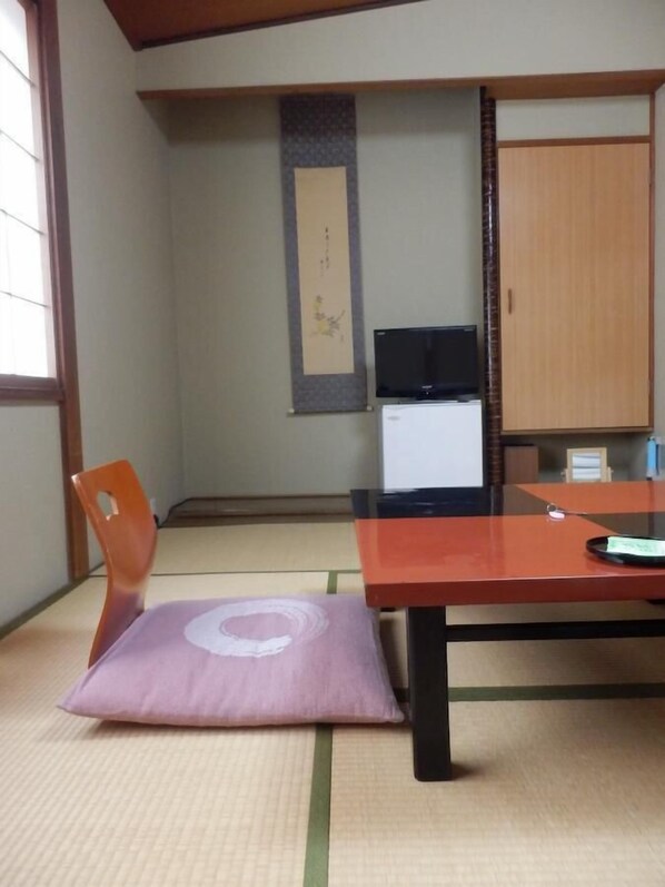 A tatami mat room with a wooden desk, a chair, a television, and a cabinet.