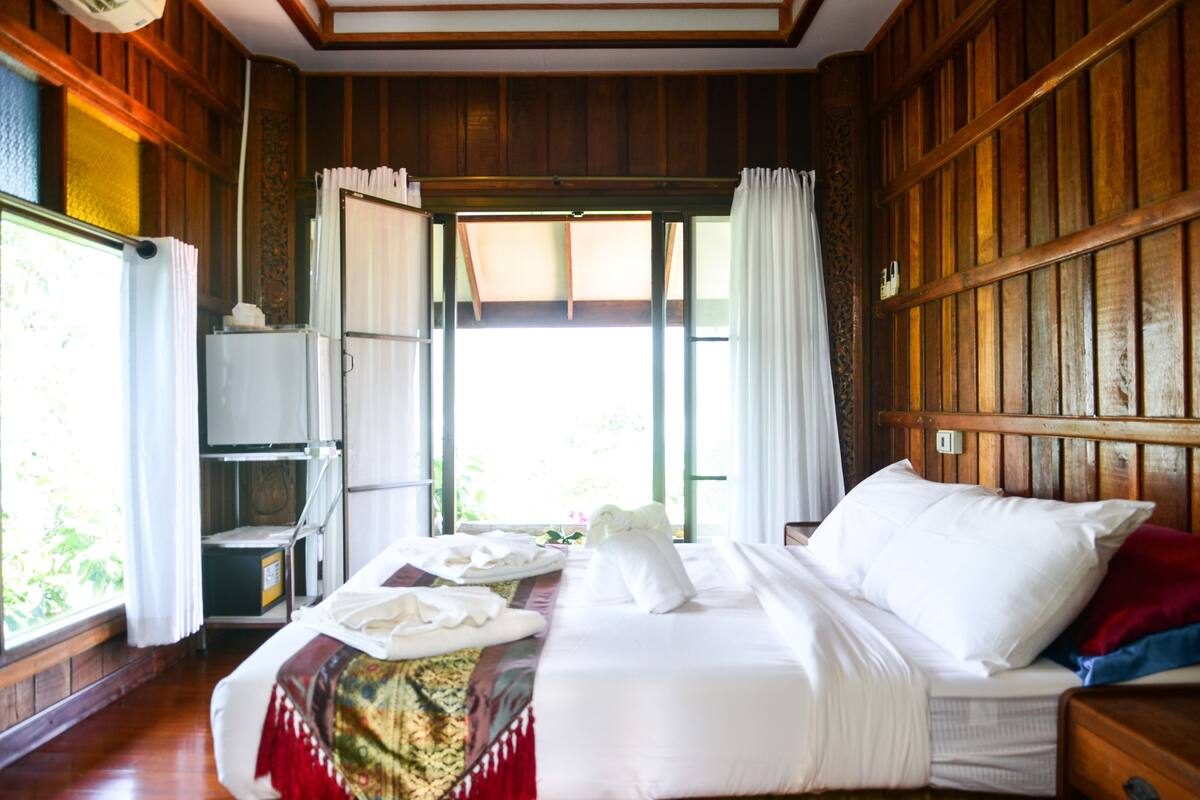 A wooden-paneled room with a bed, a small table, and a window with curtains.