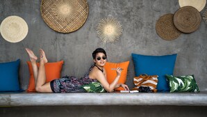 A person lying on a bench with a notebook, surrounded by colorful pillows and woven baskets on a gray wall. - Bhuvarin Resort (Ko Chang)