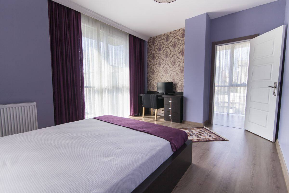 A bedroom with a bed, a desk, a chair, a television, and a door.