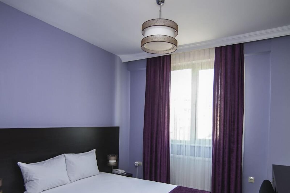 A modern bedroom with a large bed, a desk, and a ceiling light fixture.