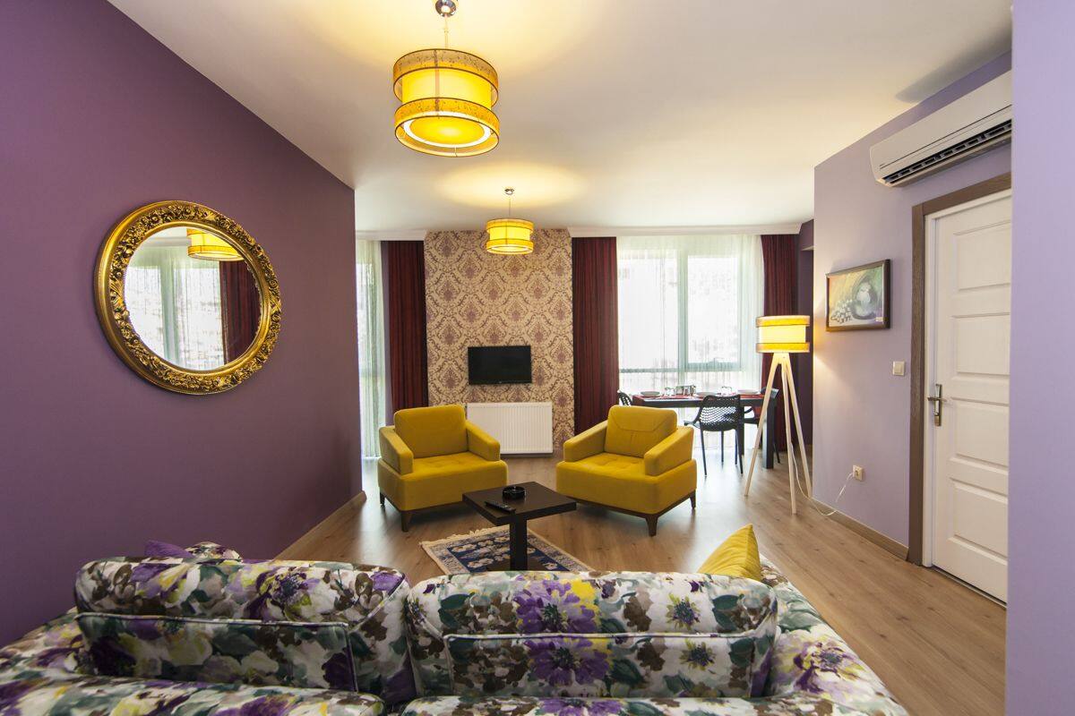 A living room with a sofa set, two yellow armchairs, a coffee table, a large mirror, and a television.