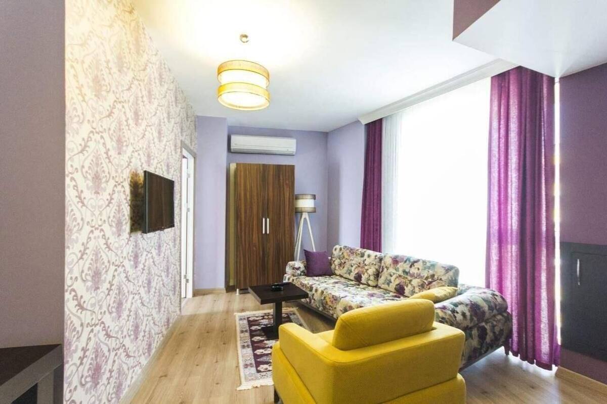 A living room with a sofa, a yellow armchair, a lamp, and a window with purple curtains.