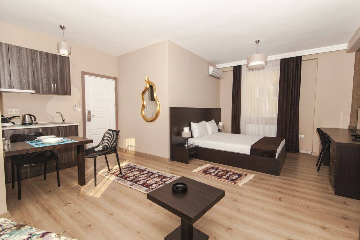 A hotel room with a bed, a desk, a chair, a small table, a mirror, and a window with curtains.
