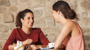 Dos personas sentadas en una mesa de madera con un muro de piedra al fondo.