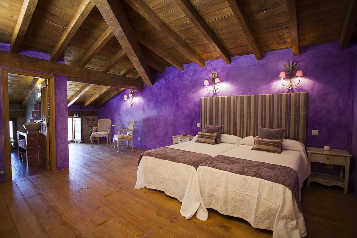 A bedroom with two beds, wooden beams, purple walls, and a wooden floor.