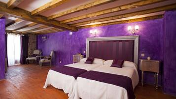 A room with two beds, wooden beams, purple walls, and a stone wall.