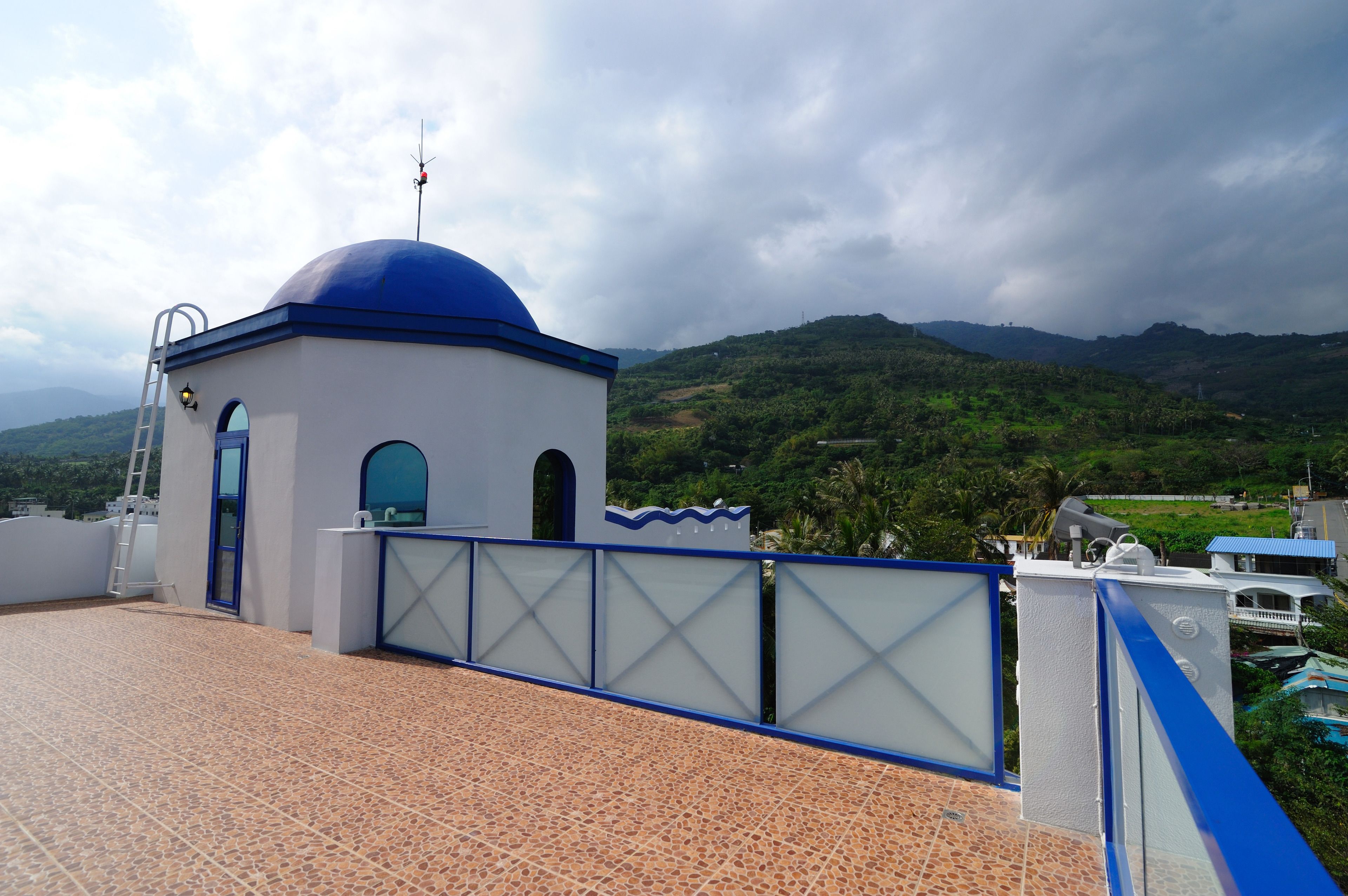 A building with a blue dome, a ladder, and a view of green hills.