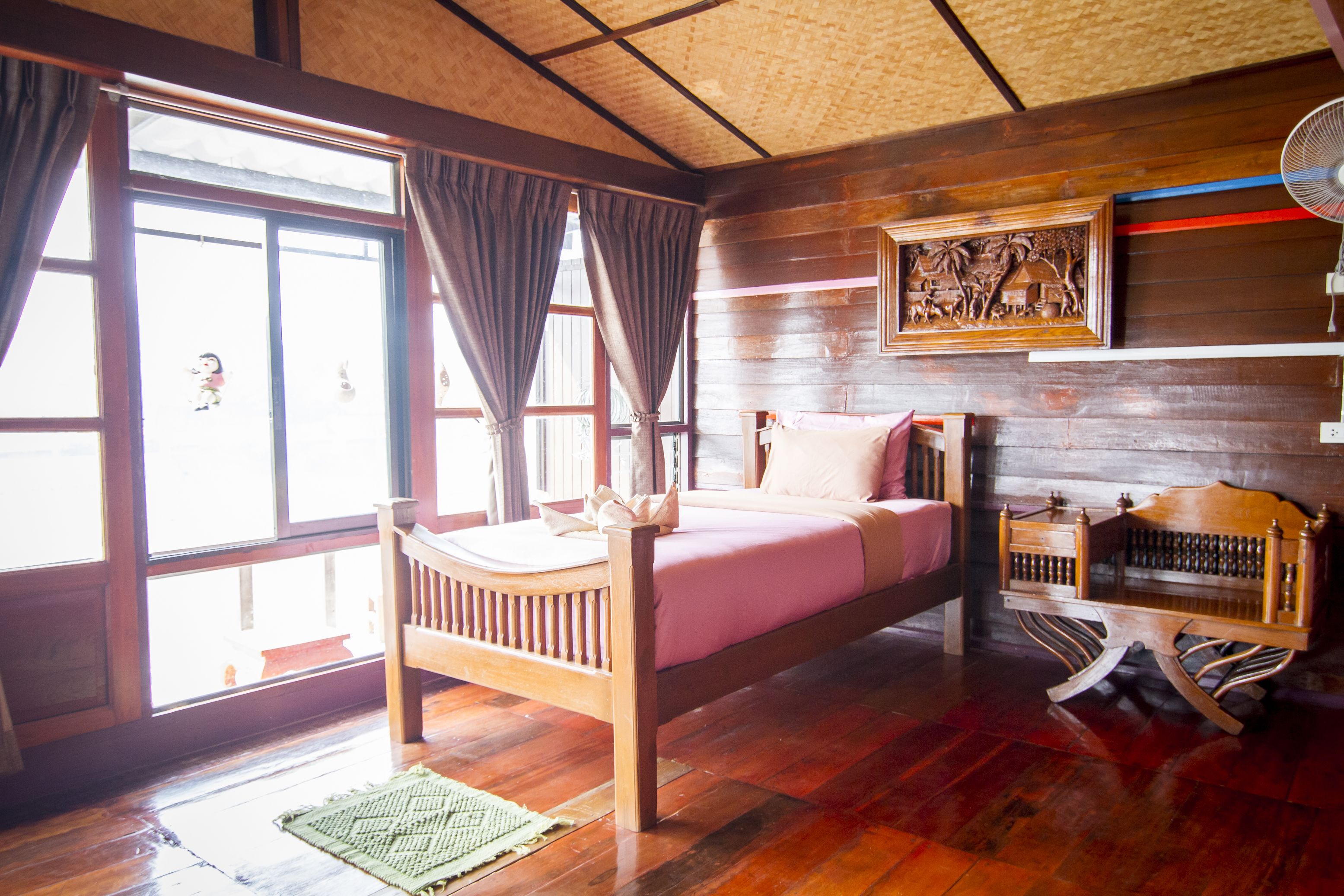 A wooden room with a bed, a nightstand, and a wall-mounted fan.