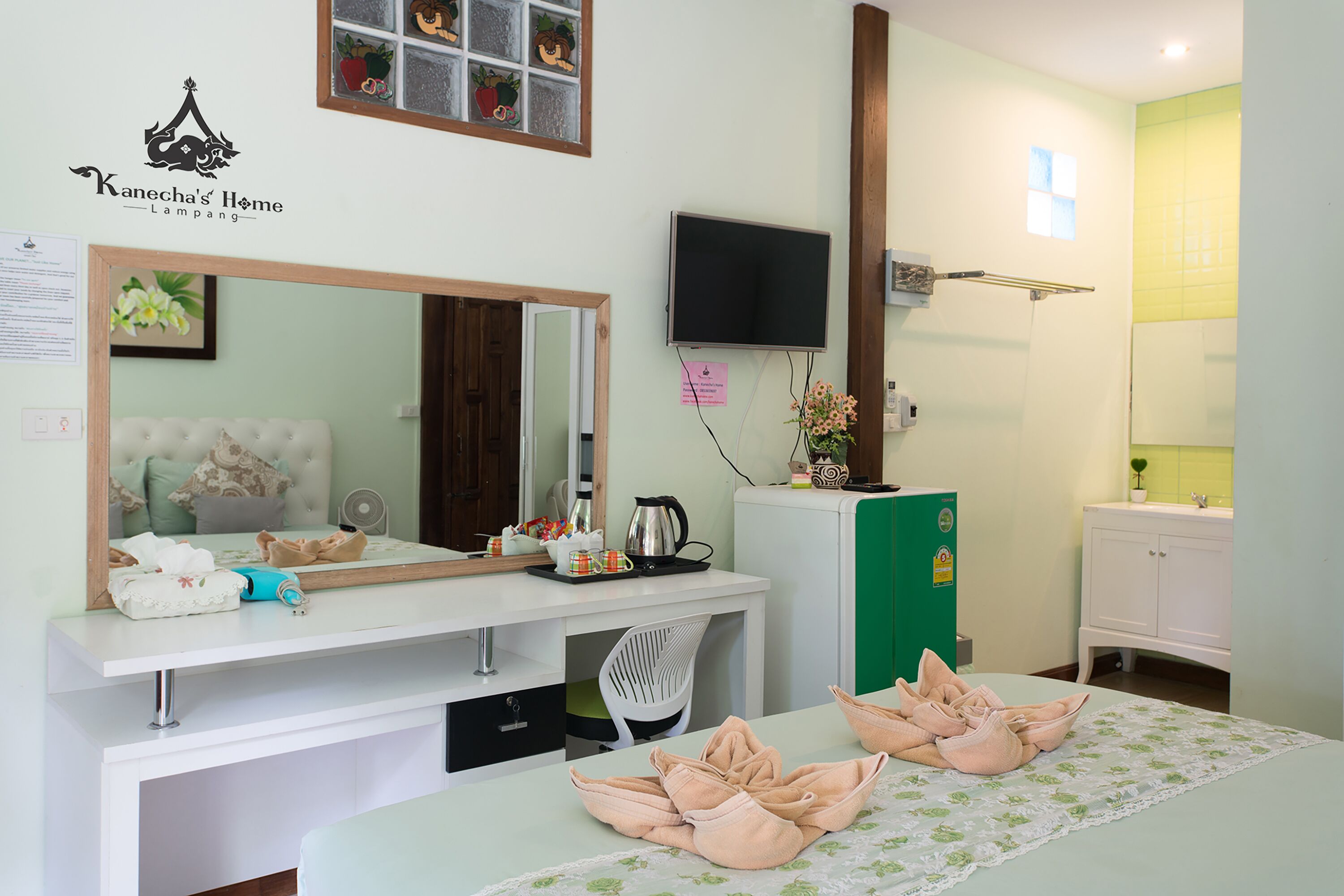 A hotel room with a bed, a desk with a mirror, a television, and a green cabinet.