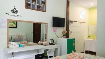 A hotel room with a bed, a desk with a mirror, a television, and a green cabinet.