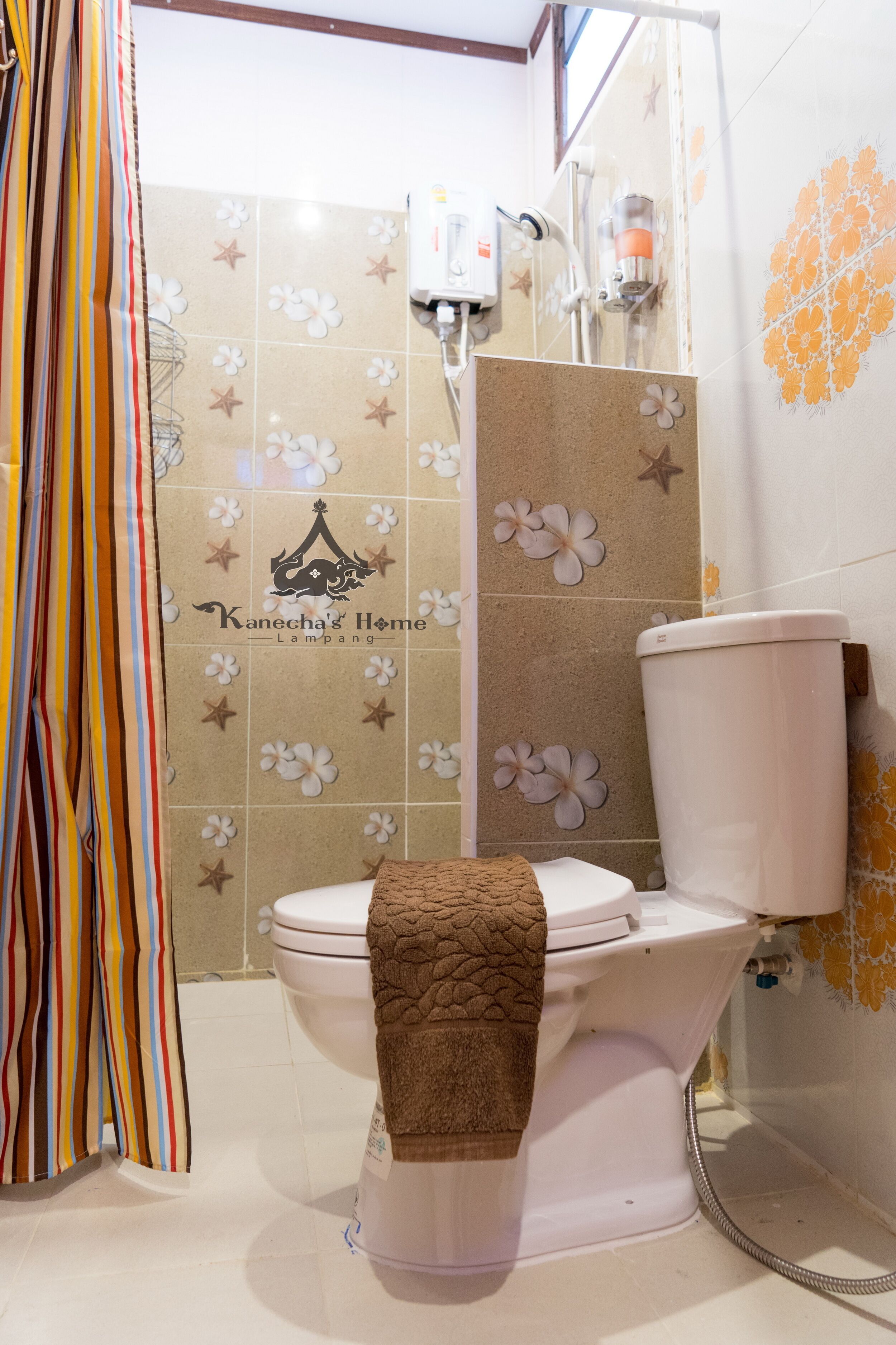 Un baño con inodoro, ducha y paredes de azulejos con diseños florales.