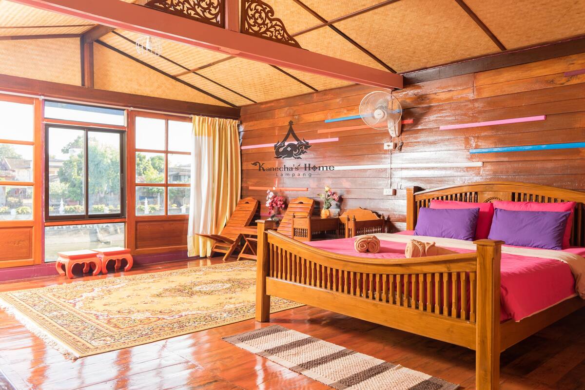 A wooden bedroom with a bed, a fan, and a large window.