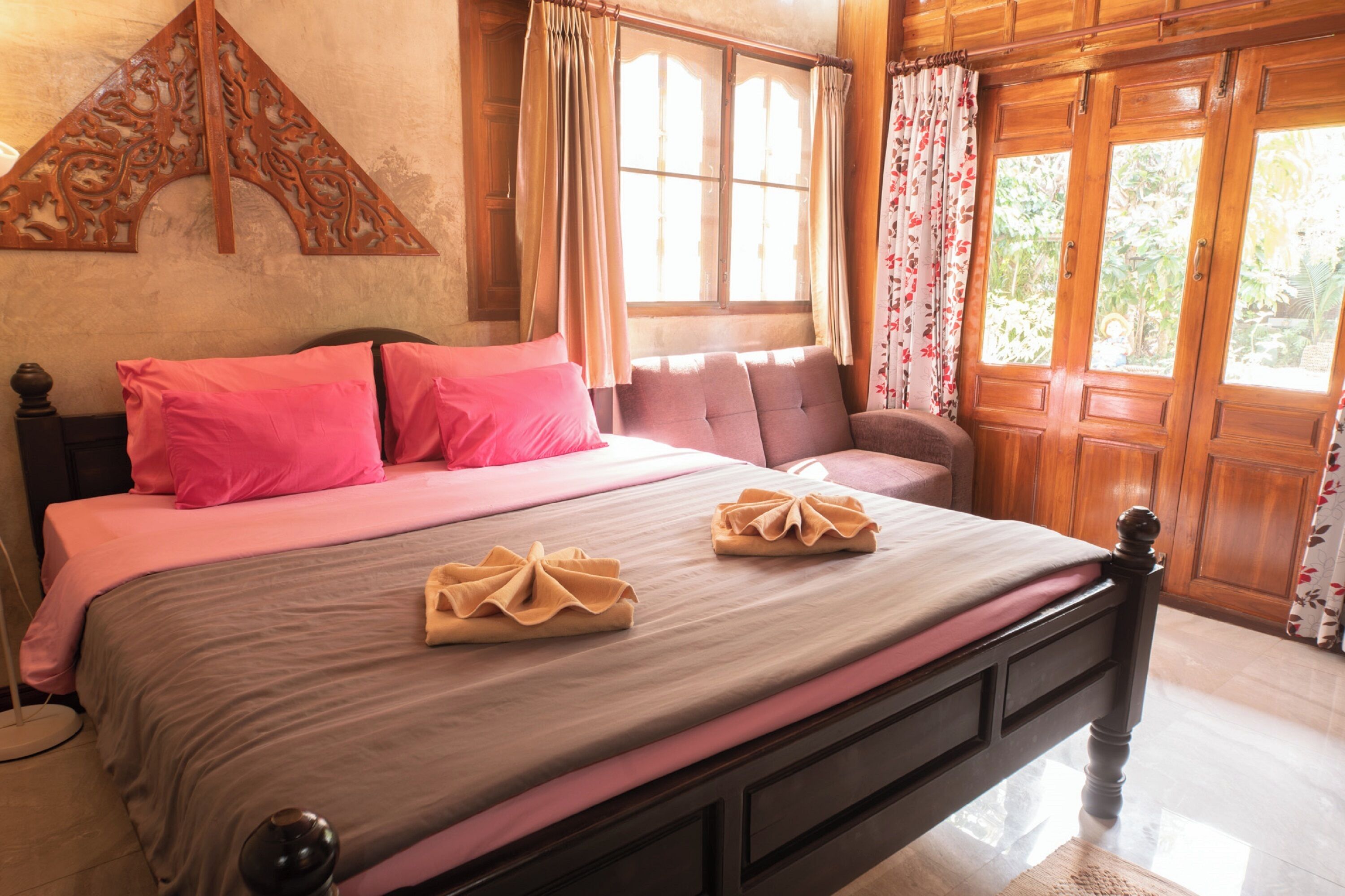 A neatly made bed with pink and beige bedding, a wooden headboard, and a decorative wall piece.