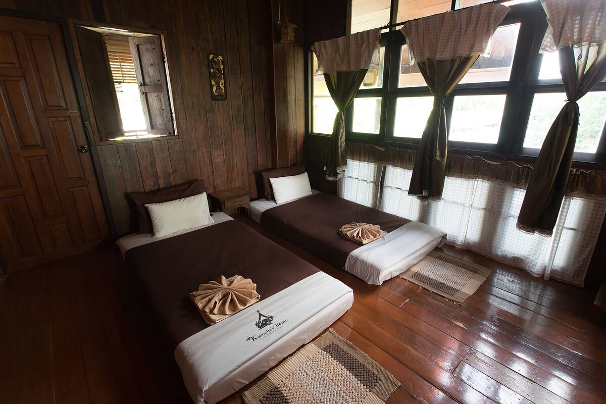 A room with two beds, wooden floors, and a window with curtains.