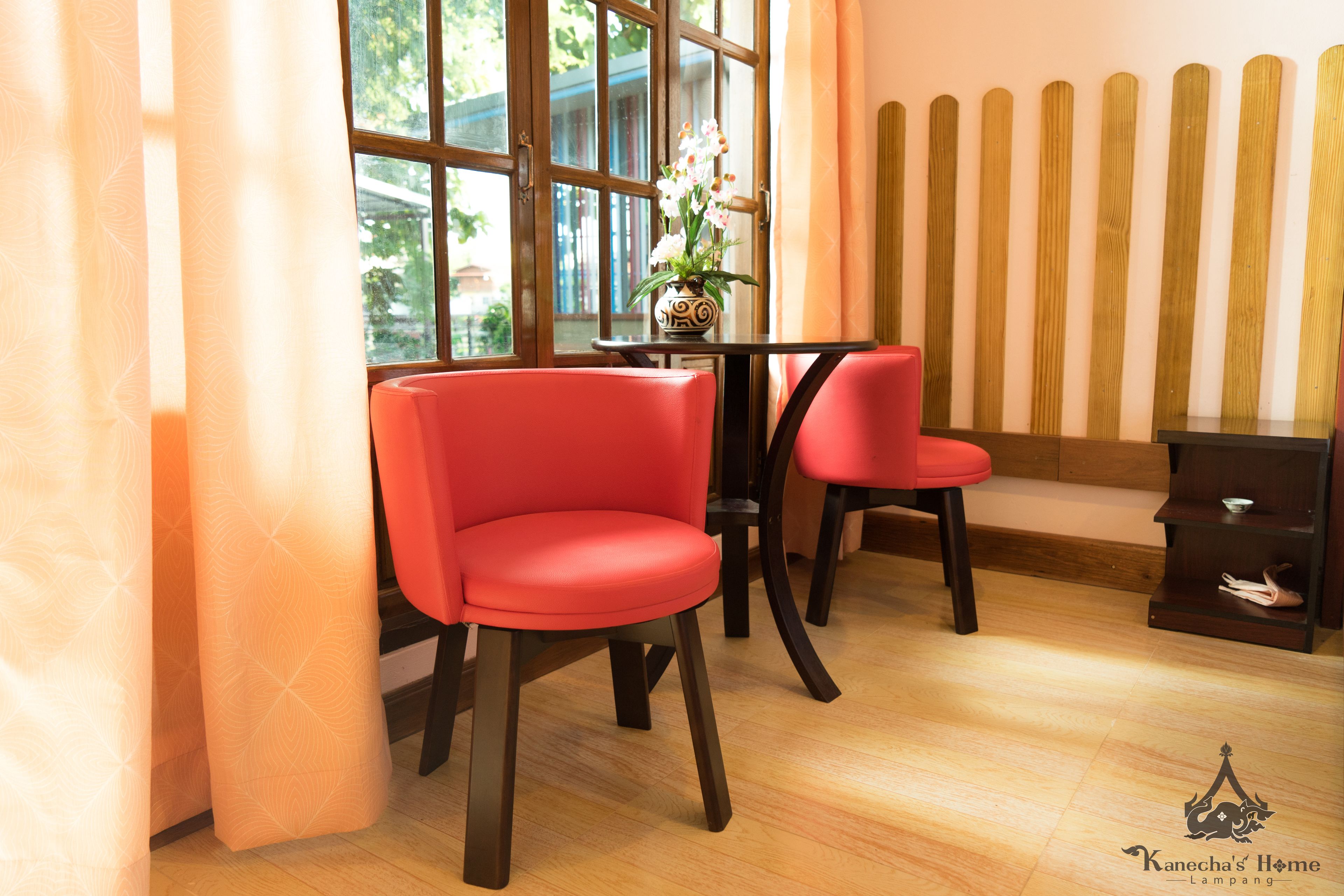 Une pièce avec deux chaises rouges, une petite table sur laquelle est posé un vase de fleurs, et une clôture en bois en arrière-plan.