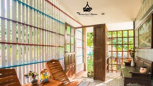 A room with wooden furniture, a wooden door, and a view of greenery outside. - Kanecha's Home (Lampang)