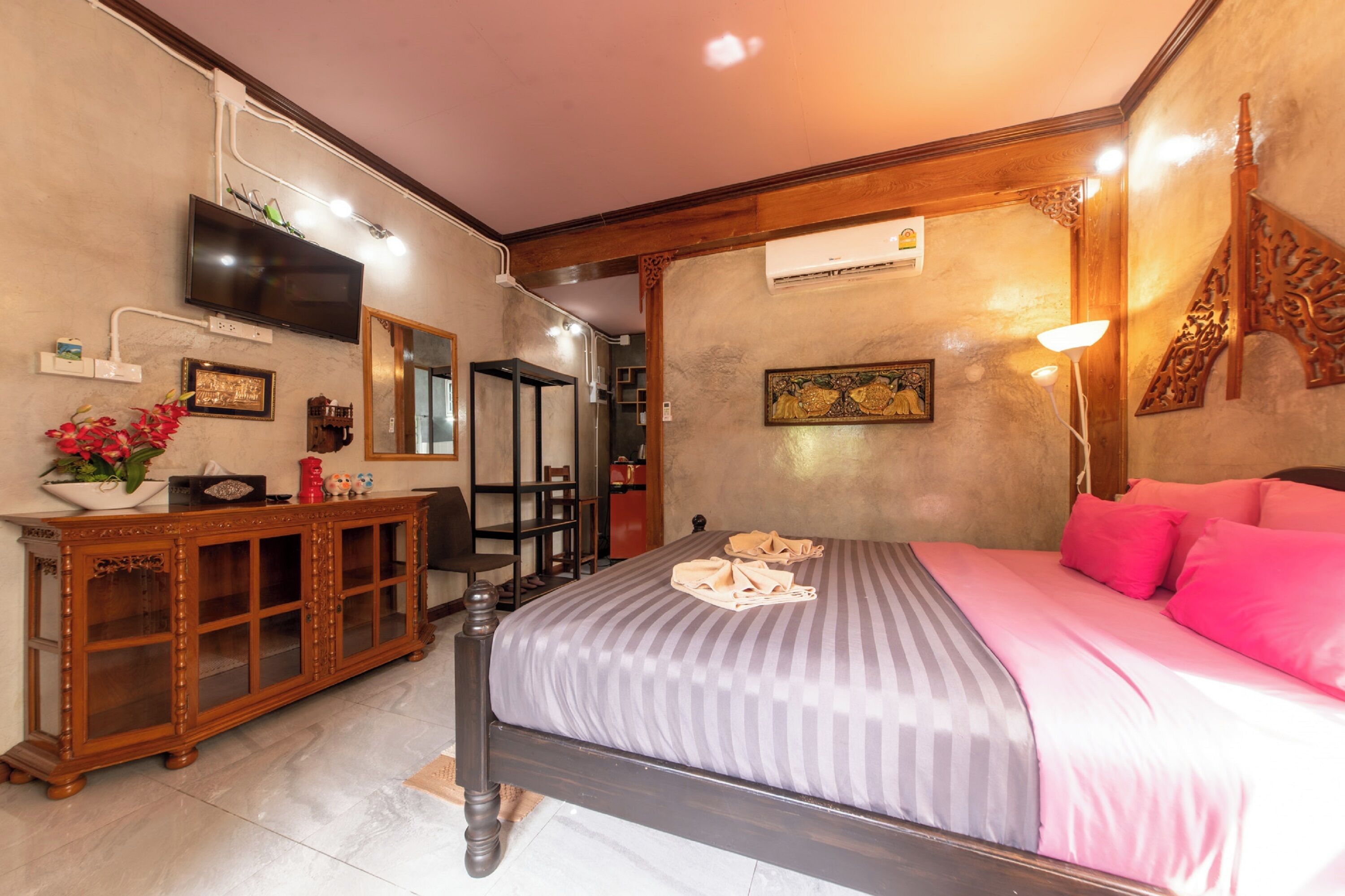 Une chambre à coucher comprenant un lit, une commode en bois, un téléviseur et un climatiseur fixé au mur.