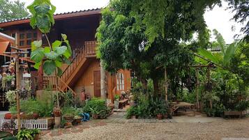 Une maison en bois avec un escalier menant à un balcon, entourée de plantes en pot et d’un chemin de gravier.