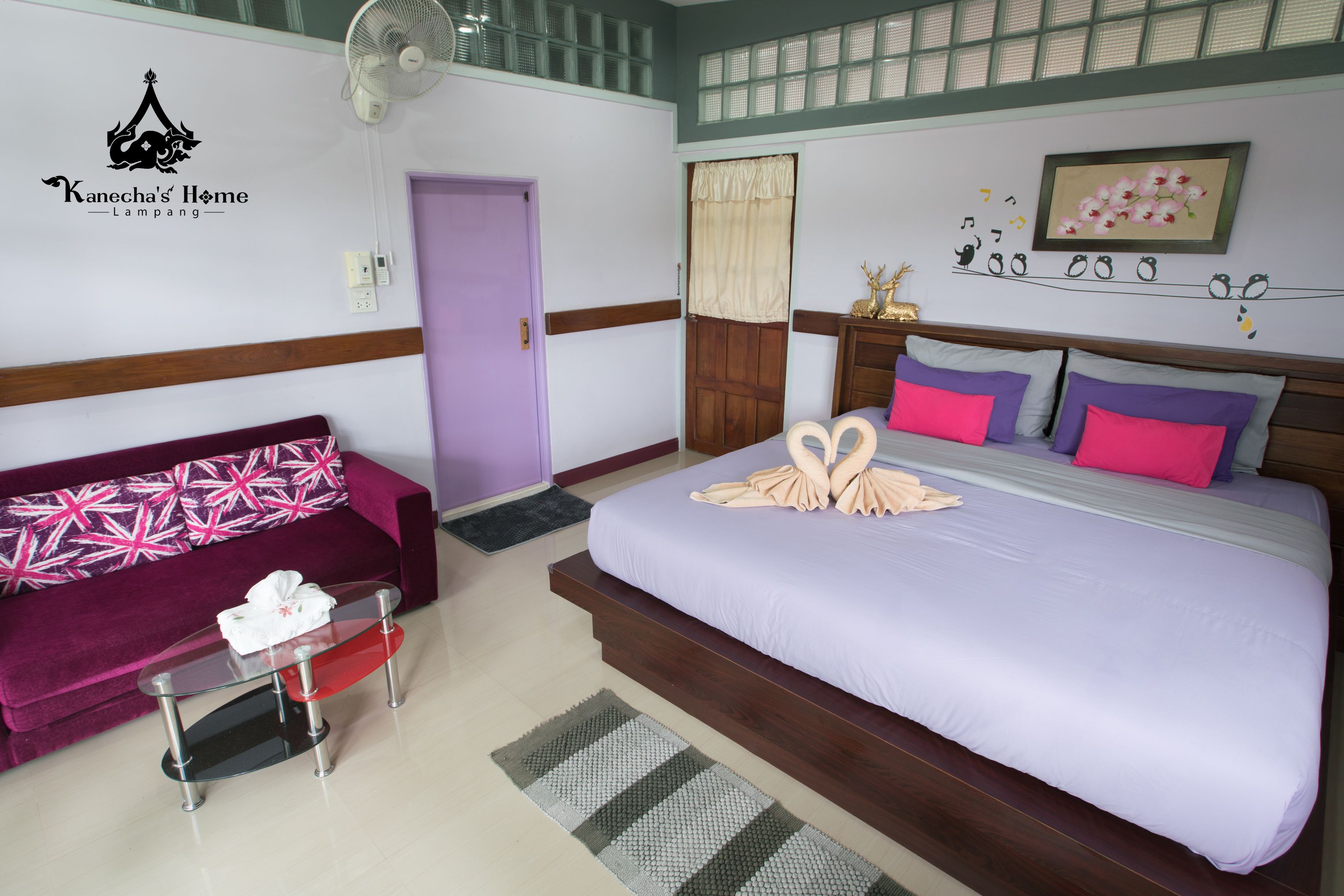 Una habitación de hotel con una cama, un sofá, una mesita, un ventilador y una puerta.