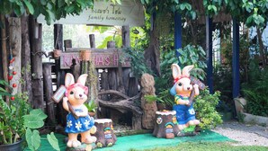 A rustic garden with two rabbit statues, wooden signage, and lush greenery. - Kanecha's Home (Lampang)