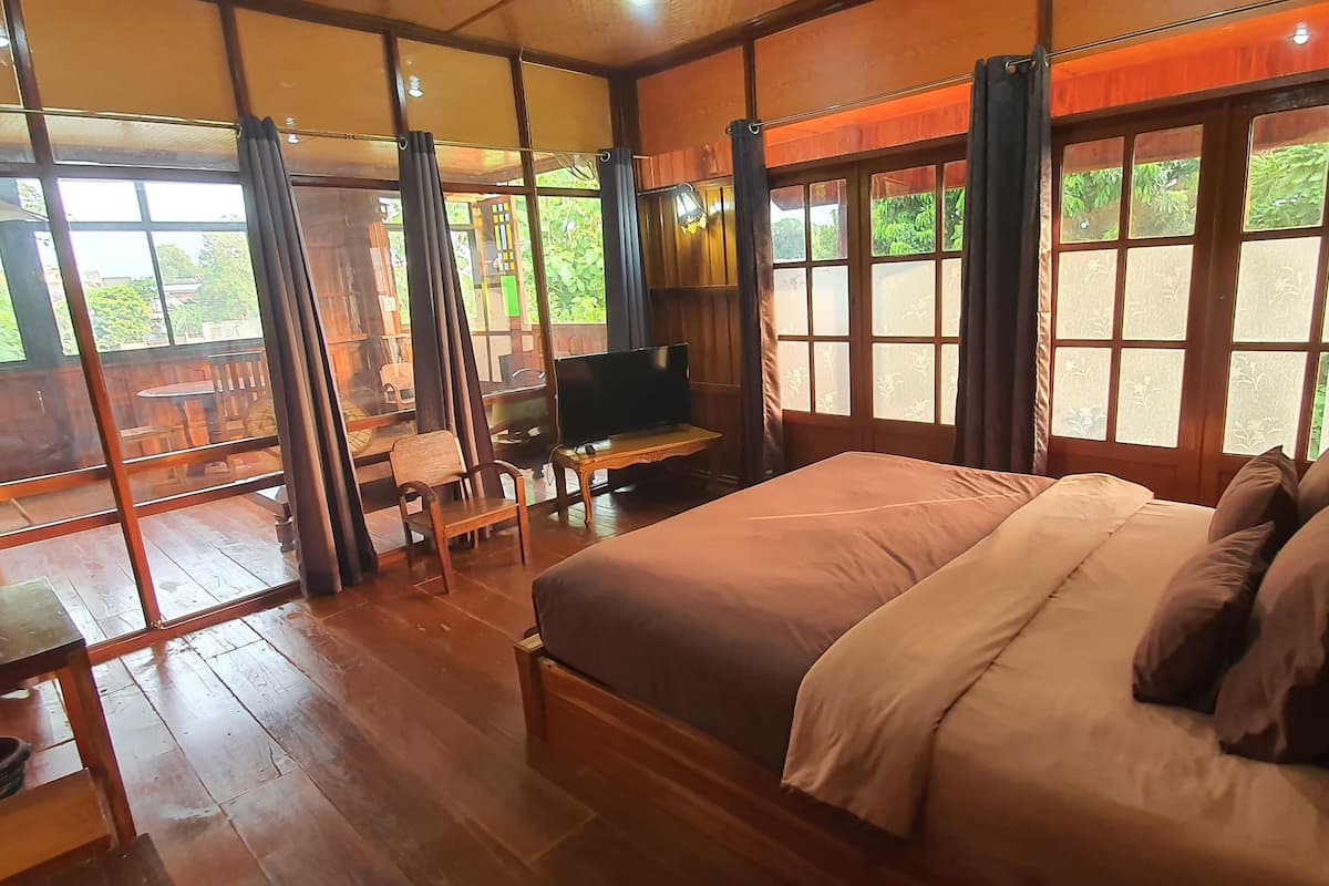 A room with a bed, a desk, and a TV. There are large windows with curtains.