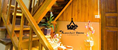 A wooden staircase with a handrail, a potted plant, and a sign reading "Kanecha's Home Lampang".