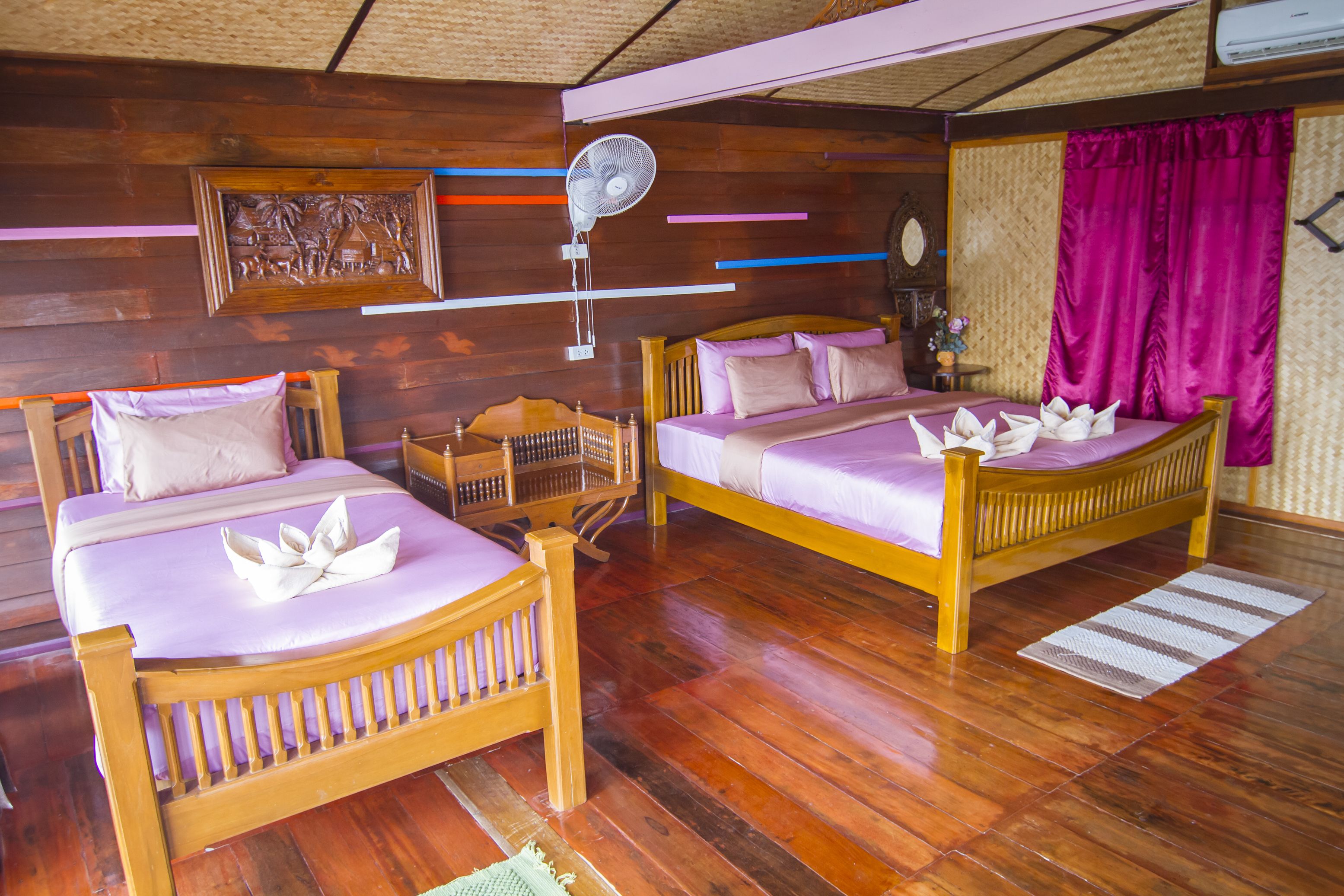 Ein Zimmer mit zwei Holzbetten, einem Deckenventilator und Holzboden.