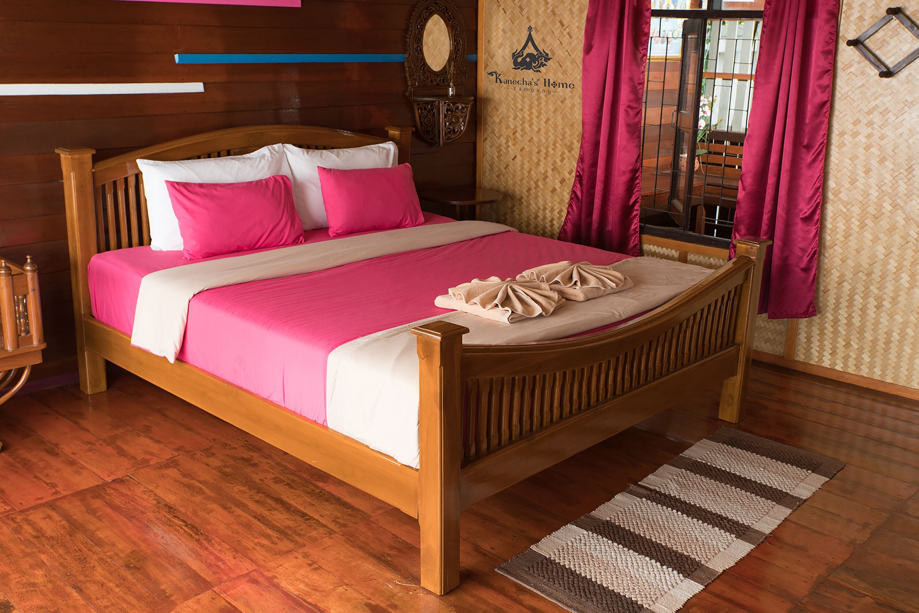 Een houten bed met een roze en witte dekbedovertrek, een houten hoofdbord en een nachtkastje met een lamp.