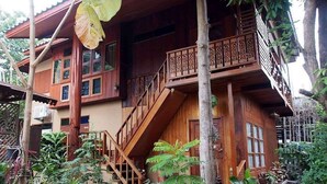 A wooden house with a balcony, stairs, and a large leaf hanging from the roof. - Kanecha's Home (Lampang)